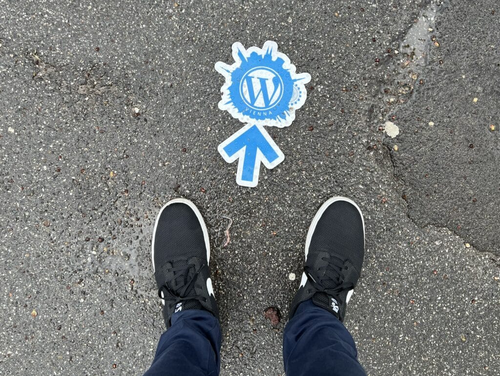 Photo of a WordCamp Vienna Logo on the floor next to a pair of black shoes.