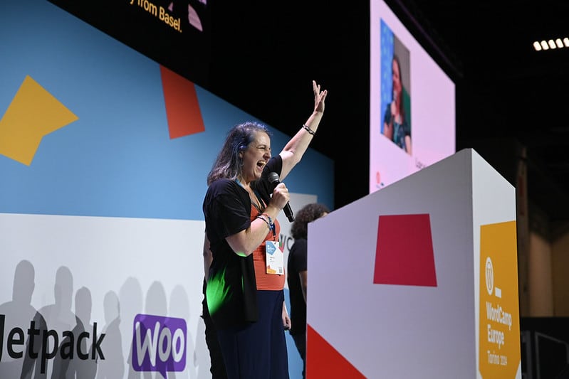Photo of Patricia on stage during the WCEU24 closing remarks. She's cheering with a microphone in her hand.